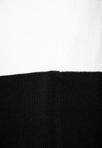 Sweter w czarno-białe paski, z miękką dzianiną, charakteryzujący się wyraźnym kontrastem kolorów pomiędzy górną białą częścią a dolną czarną częścią.