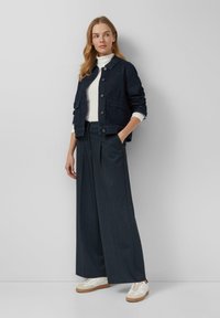 Dark denim jacket with buttons and two front pockets, paired with wide-legged trousers and white knitted top, complete with casual sneakers.
