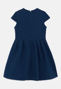 Μπλε φορέμα σε ναυτικό μπλε χρώμα με υφή υφάσματος, μανίκια τύπου καπ, εφαρμοστό μπούστο και φουσκωτή φούστα, με κλείσιμο στο πίσω μέρος με φερμουάρ.