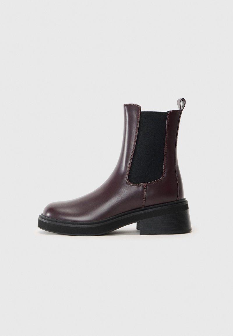Botte Chelsea en cuir bordeaux foncé avec panneau latéral élastique noir, languette, semelle épaisse noire et petit talon bloc sur fond blanc.