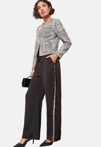 Melnbalts houndstooth īsais žakets ar zeltītēm pogām, saskaņots ar melniem platu kāju biksēm ar sudraba sānu detaļu un melnām augstpapēžu kurpēm.