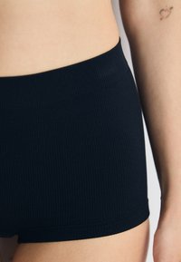 Black ribbed shorts with a smooth waistband. The fabric has a soft texture and a fitted shape, showing a slight sheen in the light.