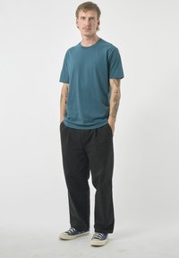 Türkises Rundhalsausschnitt-T-Shirt, kurze Ärmel, kombiniert mit schwarzen Hosen und blauen Canvas-Schuhen mit weißen Sohlen. Glatte Textur, lässige Passform.