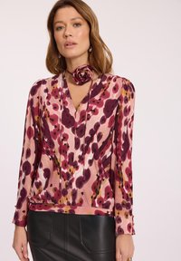 Kobieta ubrana w różowo-fioletową bluzkę z długim rękawem w wzory, z chokerem w formie różanej tkaniny, w połączeniu z czarną skórzaną spódnicą.