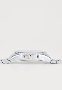 Montre en métal argenté avec une lunette polie, trois poussoirs sur le côté et un bracelet en maillons métalliques, mettant en avant un design minimaliste.