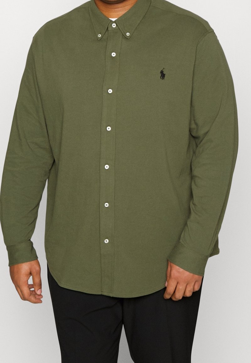 Koszula z długim rękawem w kolorze oliwkowym, wykonana z bawełny, z kołnierzykiem na guziki i małym logo na piersi. Posiada białe guziki oraz zaokrąglony dół.