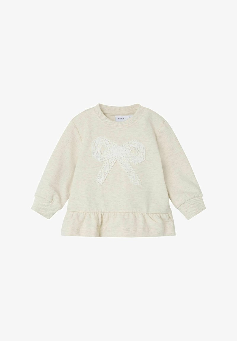 Gaišbeige džemperis ar garām piedurknēm, viļņota apakšmalu un mežģīņu loku aplikāciju centrā. Mīksta tekstūra un noapaļots kakls.