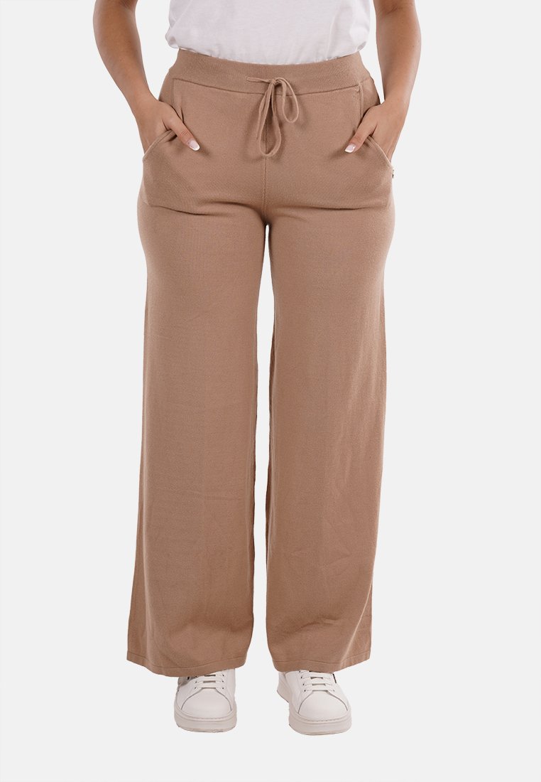 Pantaloni beige a gamba larga con vita regolabile, due tasche laterali e texture liscia, abbinati a sneakers bianche.