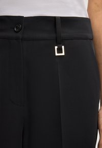 Zwarte broek met een gladde, gestructureerde oppervlakte. Beschikt over een knoopsluiting en een vierkante metalen accent op de riemlus. Eenvoudig ontwerp.