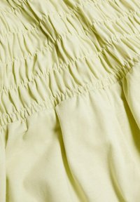 Tissu jaune clair avec une texture froncée, comportant des motifs de smocks horizontaux et un drapé doux pour plus de volume et de fluidité.