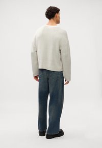 Lys grå strikket genser med avslappet passform og senkede skuldre, kombinert med høytlivede blå jeans og svarte, kraftige støvler. Det er ingen synlige mønstre.