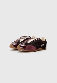 Sneaker in pelle maroon e nera con accenti testurizzati, lacci bianchi e suola in gomma. Presenta una finitura liscia e cuciture distintive.