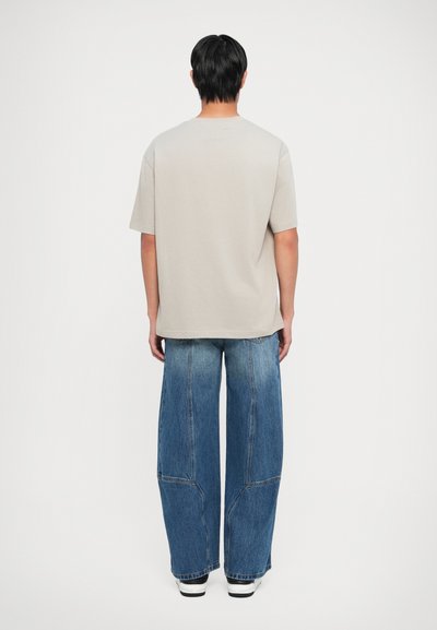 Beige bomull T-skjorte med korte ermer og rund hals, kombinert med vide blå denimjeans med synlige sømmer og lommer.