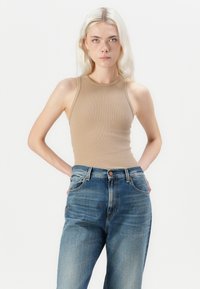 Beige geribbelde tanktop gecombineerd met hoge taille blauwe spijkerbroeken. De tank heeft een aansluitend ontwerp en een mouwloze snit.