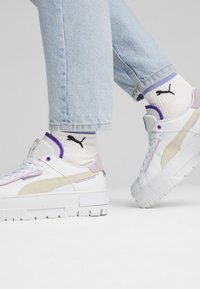 Sneaker bianche con accenti viola e beige, suola testurizzata e collo imbottito. Indossate con jeans azzurri e calzini con logo Puma.