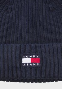 Navy strikket lue med ribbestruktur og brettet oppkant. Har et rektangulært stoffmerke med "TOMMY JEANS" og en rød-hvit-blå logo.