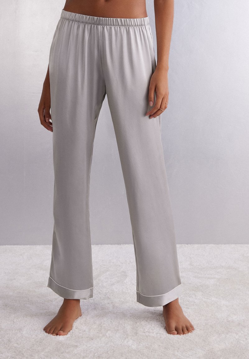 Lichtgrijze, satijnachtige pyjama's met een elastische tailleband en brede benen. De manchetten hebben een contrasterende zijden afwerking. Zachte textuur.