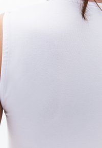 Witte mouwloze top met een gladde textuur, een aansluitend ontwerp en minimale stikdetails. Het materiaal lijkt zacht en lichtgewicht.