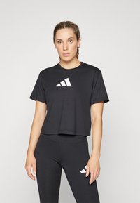 Svart cropped t-skjorte med rund hals og korte ermer, med en hvit diagonalt stripe-logo på brystet. Sorte leggings med matchende logo.