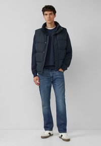 Granatowa pikowana kamizelka z zatrzaskiem, noszona na teksturowanej granatowej bluzie. Dobranie do niebieskich dżinsów i białych tenisówek z szarymi akcentami.