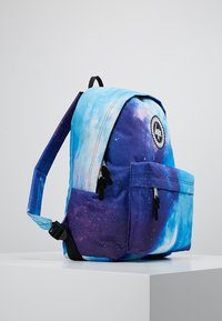 Reppurekko sinisessä ja purppurassa galaksikuviossa, jossa on etutasku, säädettävät hihnat ja logo-ompelu sivussa. Teksturoitu kangas.