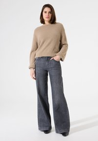 Beige, textuur, langenaam trui gecombineerd met grijze, hoge taille, wijde jeans. De outfit heeft minimale accenten en effen kleuren.