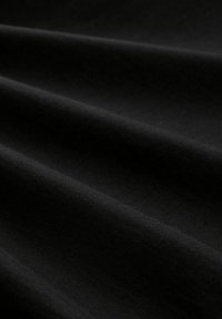 Zwart katoenstof met een soepele textuur, met subtiele draperingen en plooien, die de flexibele en ademende kwaliteiten benadrukken.