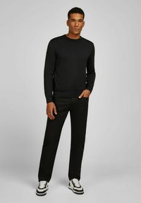 Zwarte crewneck trui met geribde manchetten en onderrand, gecombineerd met zwarte broek en zwart-witte sneakers. Soepele stof met een aansluitend ontwerp.