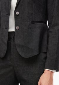 Dopasowany czarny garnitur z teksturowanej tkaniny z subtelnym wzorem. Marynarka ma dwa guziki i jedną kieszeń na piersi.
