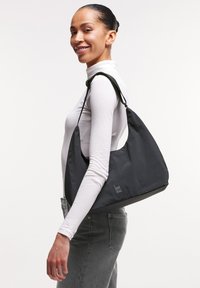 Borsa a spalla nera realizzata in tessuto resistente, con una forma curvada, una tracolla regolabile singola e un logo visibile.