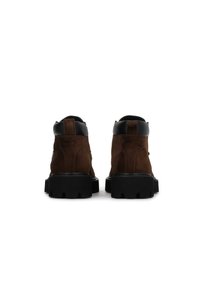 Ghete ankle din suede maro, cu un guler din piele neagră, talpă din cauciuc negru solid și o bucată de prindere în spate. Design simplu cu șireturi în față.
