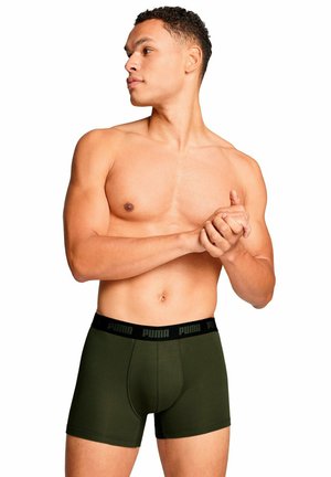Boxer da uomo di un verde scuro con un elastico nero che presenta il logo Puma. Il tessuto sembra liscio e elastico. Modello in piedi con le mani unite.