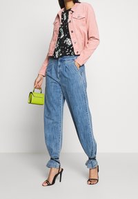 Pink corduroy jakke, sort blomster top, afslappede lyseblå jeans med snore ved manchetterne, og sorte hæle sandaler. Grøn mini håndtaske som accent.