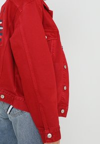 Veste en denim rouge au design ajusté. Dispose de fermetures à boutons argentés sur le devant et les poignets. Couture contrastante visible.