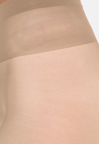 Transparent strumpor i hudtoner, med en slät textur och en gradientdesign som går från ljusare till mörkare vid midjan.