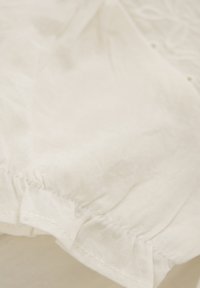 Witte katoenstof met een gestructureerd oppervlak, voorzien van een gathered zoom. Zacht en met een licht kreukelig uiterlijk en een subtiele glans.