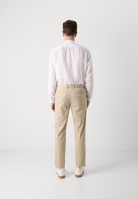 Beige chinos ar taisnu piegriezumu, apvienoti ar baltu linu krekls. Iekļauj sānu kabatas un jostu, valkāti ar baltām sporta kurpēm.