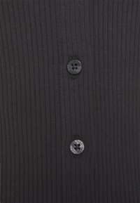 Black ribbed fabric featuring two round buttons with four holes. The texture is smooth with vertical ribbing throughout the material.
