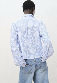 Blouse à motif floral bleu clair avec des manches bouffantes et une coupe légèrement cropped, associée à un jean en denim bleu clair.