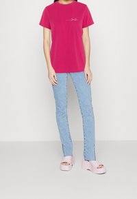 Fuchsia cotton t-shirt with short sleeves and a left chest logo. Paired with light blue jeans and light pink platform sandals.