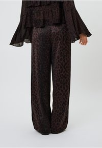 Platas kājas bikses tumšā, mirdzošā audumā ar brūna leoparda rakstu. Dizainā ir gluda, plūstoša tekstūra un brīva piegriezuma forma.