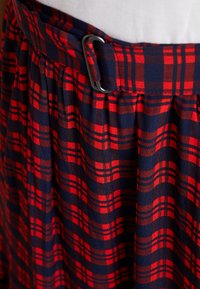 Rode en marineblauwe geruite rok met plooien, voorzien van een stoffen riem en een metalen gesp, die een gestructureerd materiaal en een gedurfde kleurcontrastering toont.