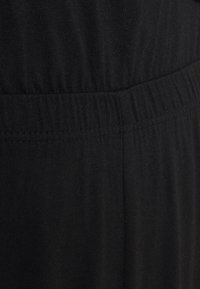 Gros plan sur un tissu noir côtelé avec une ceinture élastique et un détail de couture.