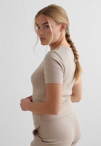Beige ribbet top med korte ærmer, rund halsudskæring, tætsiddende design og sømløs overflade, båret med matchende bukser.