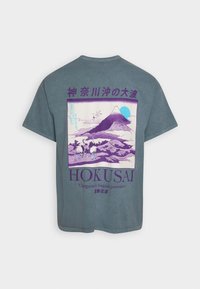 Graues T-Shirt mit einem lila Grafik von dem Berg Fuji, umgeben von Krähen, daneben japanischer Text und "HOKUSAI" darunter gedruckt. Retro-Design.
