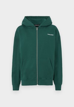 Zelená mikina na zips vyrobená z mäkkého materiálu, má kapucňu, predné vrecká a malé biele logo na ľavej strane hrude.