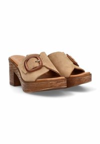 Mules de ante beige con diseño de punta abierta, que presentan una gran hebilla de madera y un tacón tipo bloque con textura similar a la madera.
