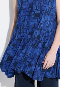 Tunica blu con motivo astratto e textures, caratterizzata da una silhouette svasata. Il tessuto è leggero e leggermente drappeggiato.