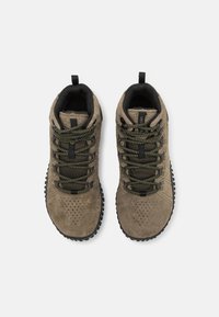 Zapatos de senderismo de gamuza marrón con detalles en negro, que cuentan con cordones texturizados en verde y negro, perforaciones en la puntera y una suela robusta.