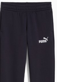 Tmavomodré tepláky s elastickým pásom a bielym logom Puma na ľavej strane. Viditeľná hladká textúra látky.